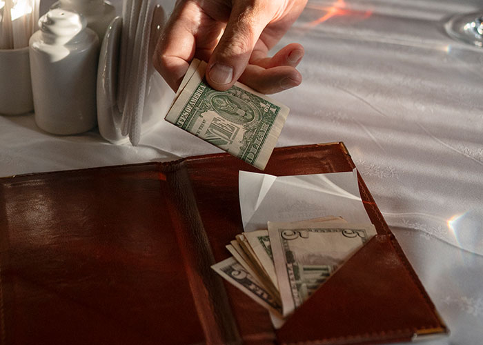 Hand tipping with folded bills in a restaurant setting, showcasing interesting facts from the community.