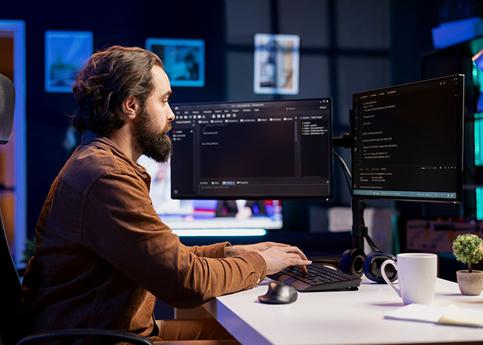 Man working at a dual-monitor setup in a modern office, focusing on coding, representing intriguing facts and learning.