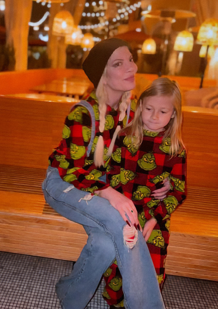 Tori Spelling with her child in matching outfits sitting on a bench in a warmly lit area.