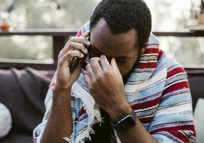 Man wrapped in a striped blanket on the phone, appearing stressed, outdoors, related to toxic family dynamics.