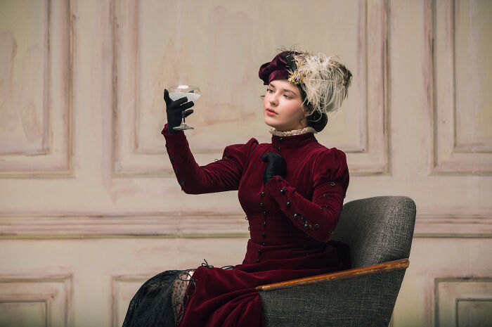 A woman in vintage attire, examining a glass, represents Pinterest’s 2025 trends predictions in a stylish setting.