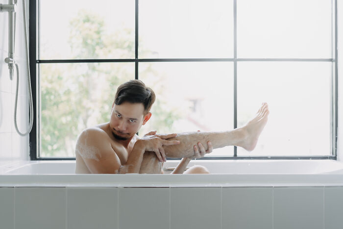 Man in bathtub surrounded by soap suds, illustrating hygiene hacks. 