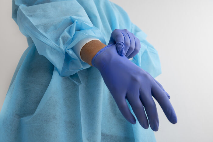 Person in a blue medical gown putting on purple gloves, illustrating hygiene hacks. 