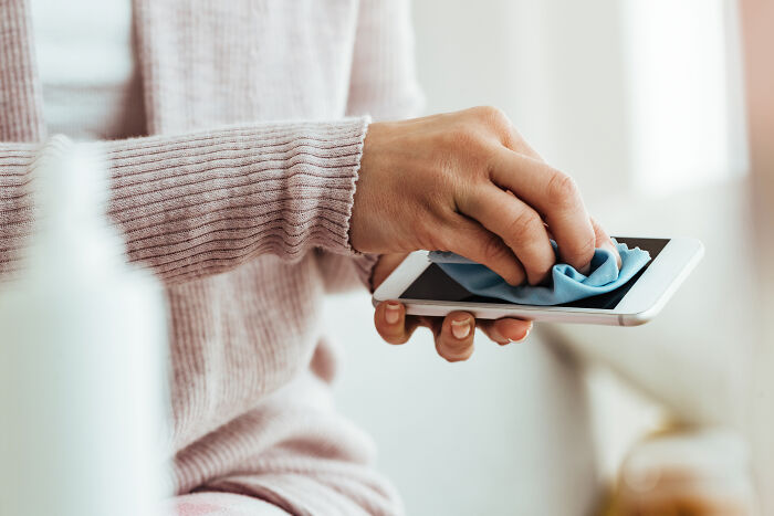 Person cleaning a smartphone screen with a cloth, illustrating hygiene hacks. 