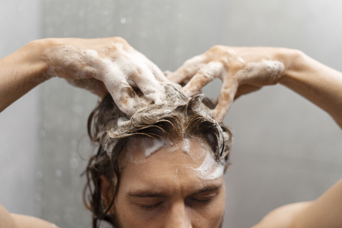 Person washing hair, applying shampoo with hands, illustrating hygiene hacks. 