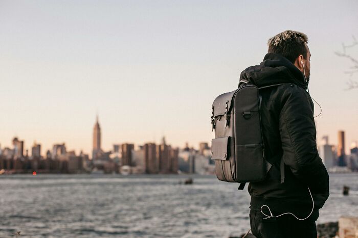 Person with a backpack gazing at a city skyline across the water at sunset, illustrating hygiene hacks.