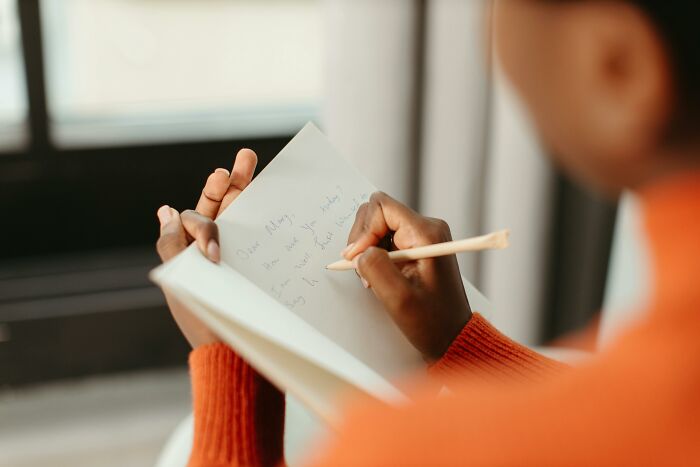 Person writes in a notebook, seated by a window, depicting vegan family concerns over neighbors cooking meat. Person writes in a notebook, seated by a window, depicting vegan family concerns over neighbors cooking meat.