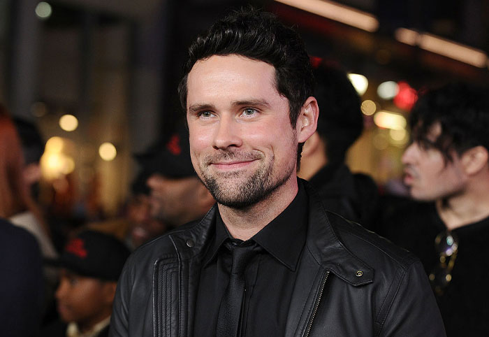 Smiling Virgin River cast member in a black leather jacket at an event, surrounded by a crowd.