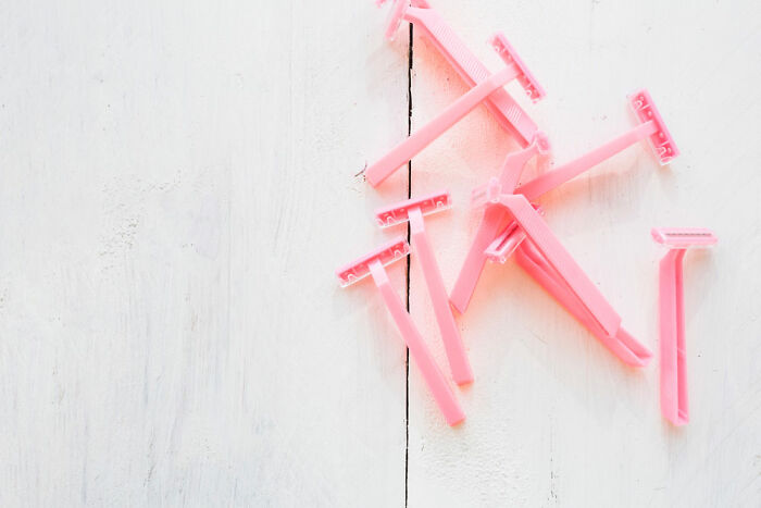 Pink disposable razors scattered on a white wooden surface.