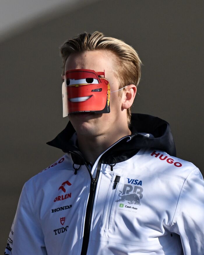 Person wearing a cartoon face mask in a humorous and bizarre setting, promoting an official social media account.