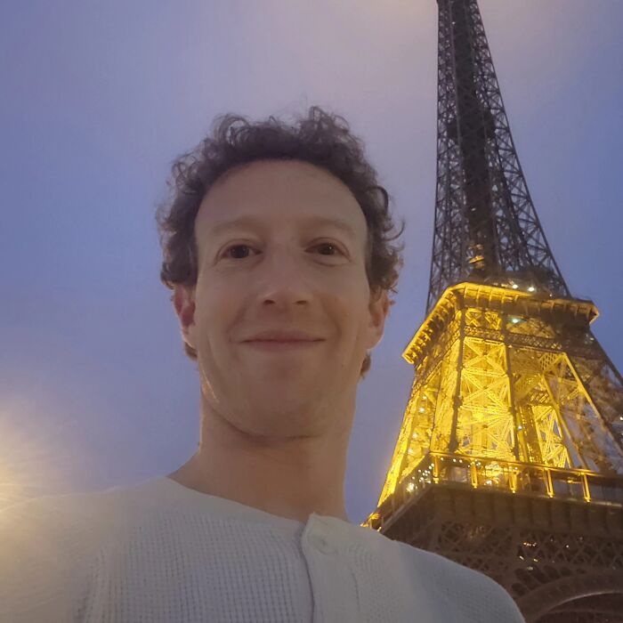 Man smiling near the illuminated Eiffel Tower at dusk, capturing a funny and bizarre moment for social media.