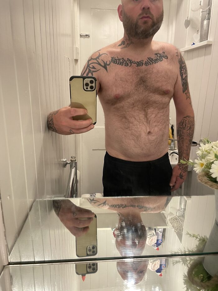 shirtless man with tattoos taking a mirror selfie in a bathroom