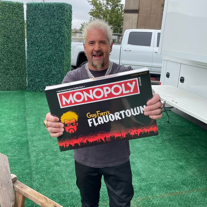 Person holding a Monopoly box themed as Flavortown, smiling outdoors; funny and bizarre social media post.