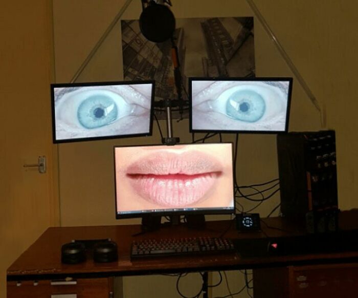 Three monitors display a pair of eyes and lips, creating a bizarre and funny setup on a desk.