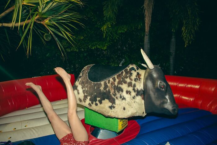 Person falling off a mechanical bull in a funny and bizarre moment, legs in the air, surrounded by inflatable ring outdoors.