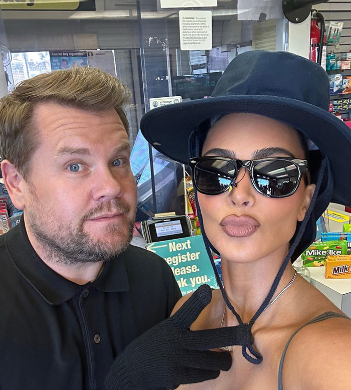 Kim Kardashian wearing sunglasses, a wide-brimmed hat, and gloves, posing for a selfie with a man in a convenience store, surrounded by candy displays.