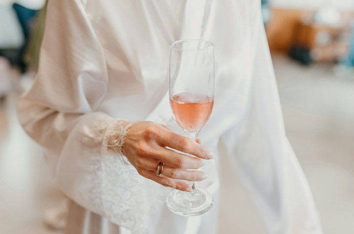 Woman in white holding a glass of rose wine, symbolizing wedding guest attire controversy.