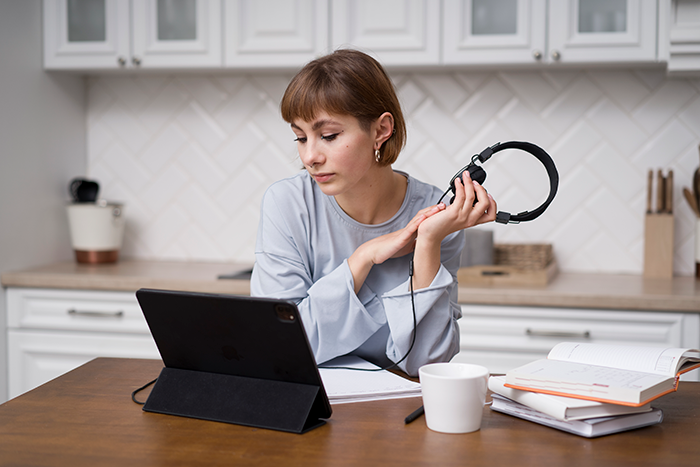 Person planning a Japan trip on a tablet, holding headphones, sitting at a desk in a kitchen setting. Person planning a Japan trip on a tablet, holding headphones, sitting at a desk in a kitchen setting.