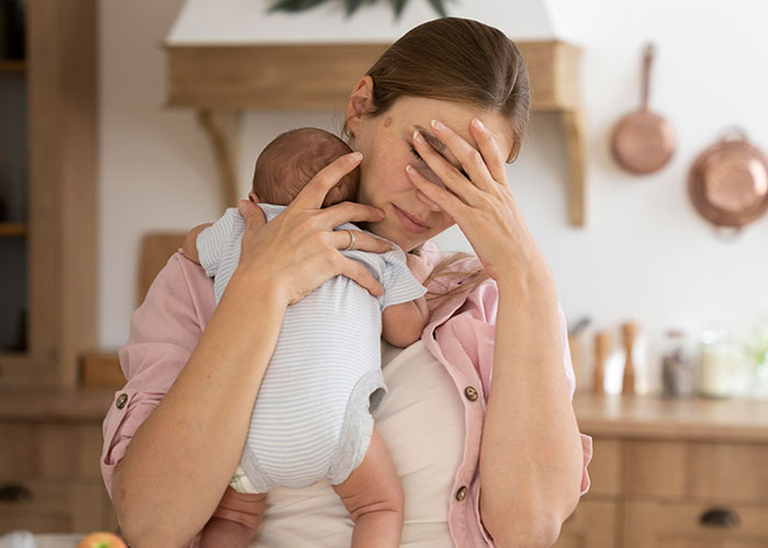 Mother holding baby, looking stressed in the kitchen, with in-laws not holding the child. Mother holding baby, looking stressed in the kitchen, with in-laws not holding the child.