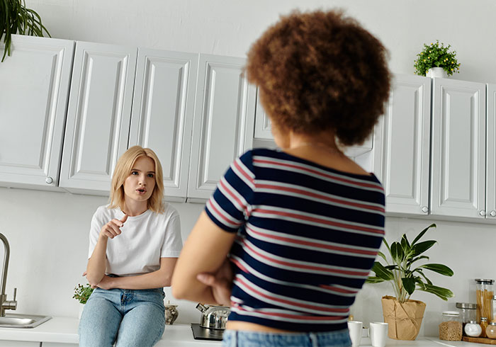 Woman sitting on kitchen counter, gesturing while talking to another person, discussing a dilemma with sister-in-law&rsquo;s kids.