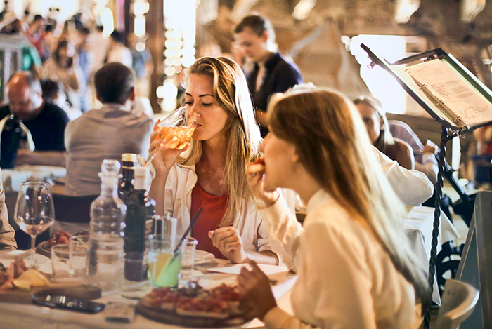 Women dining in a busy restaurant, engaged in conversation and enjoying drinks.
