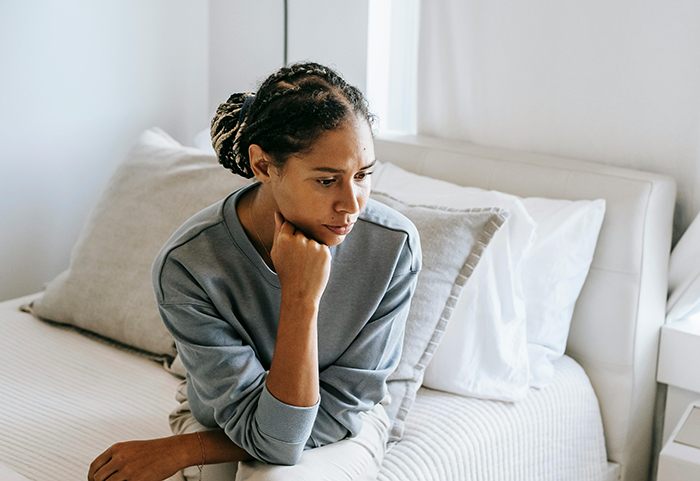 Woman sitting on a bed, looking thoughtful, highlighting dream wedding concerns.