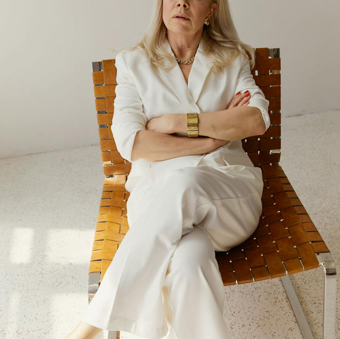 Woman in white suit sitting with arms crossed, looking displeased, highlighting MIL visiting unannounced.