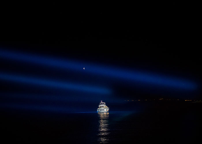 Cruise ship illuminated by spotlights on the sea at night under a crescent moon.