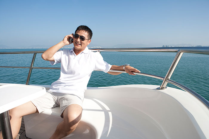 Man in a white shirt on a yacht, holding a phone, representing luxury and service to a billionaire family. Man in a white shirt on a yacht, holding a phone, representing luxury and service to a billionaire family.