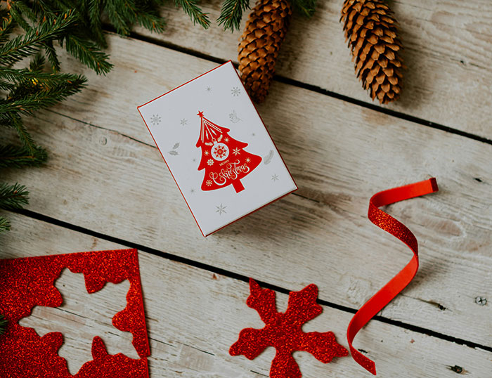 Christmas gift wrapping with tree design, pinecones, and red snowflake decorations on a wooden surface.