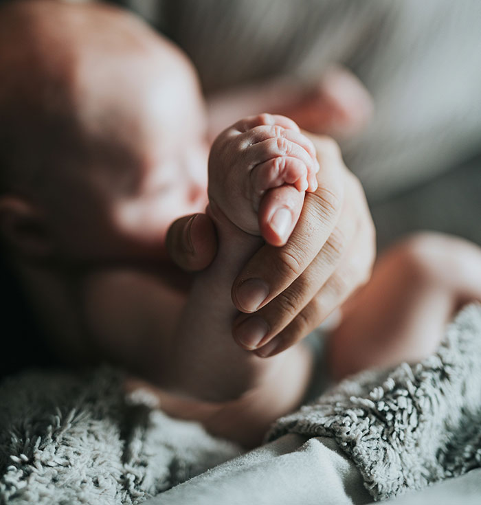 A parent gently holds a baby's hand, illustrating challenges in parenting shared by maternity employees.
