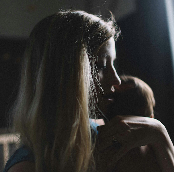 A mother holding her child in a dimly lit room, reflecting on parenting challenges.