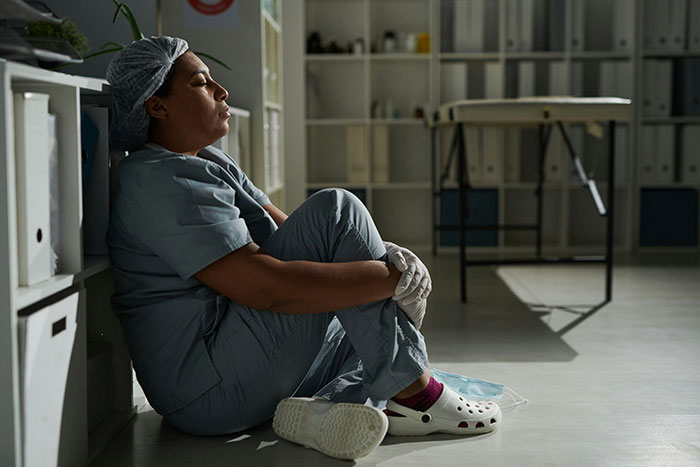 Maternity employee sitting on floor, looking exhausted in a hospital setting.