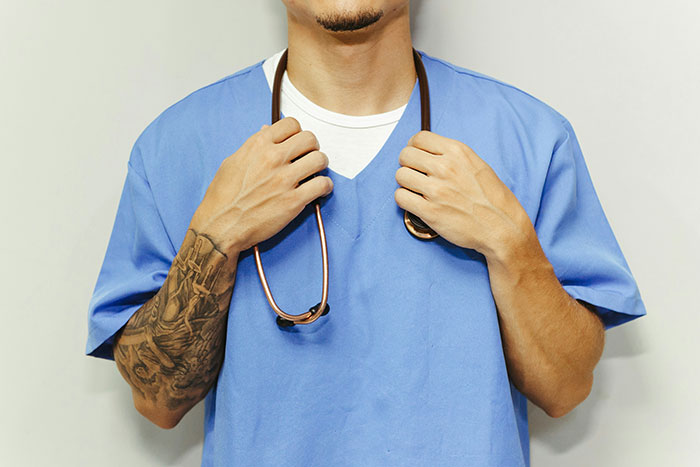 Maternity employee in blue scrubs with a stethoscope, showcasing a tattooed arm.