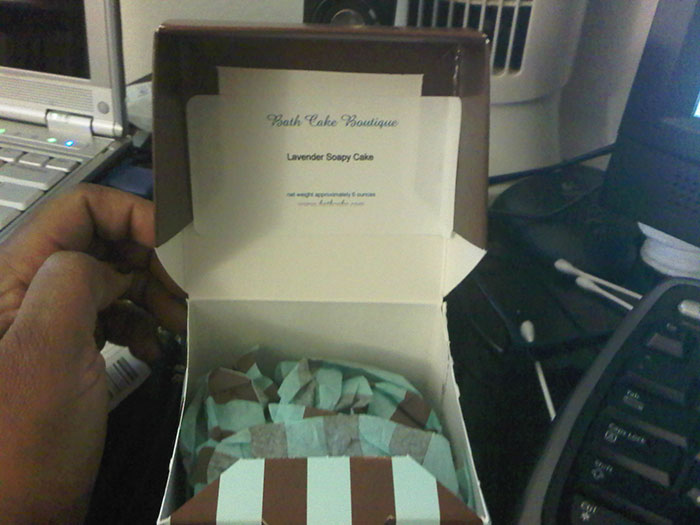 Secret Santa gift box with a humorous "Lavender Soapy Cake" label, held by a person near a computer.