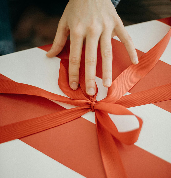 A hand opening a Secret Santa gift with a red ribbon on a striped box.