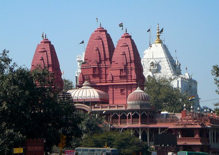 Historic red and white temple structures surrounded by trees in a city, depicting traditional architecture.