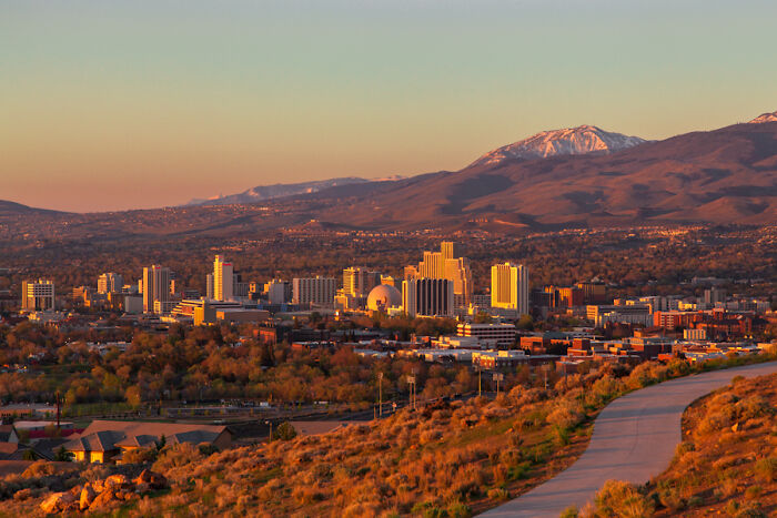 City skyline at sunset with mountains in the background, representing travel to a less favorable city-country destination.