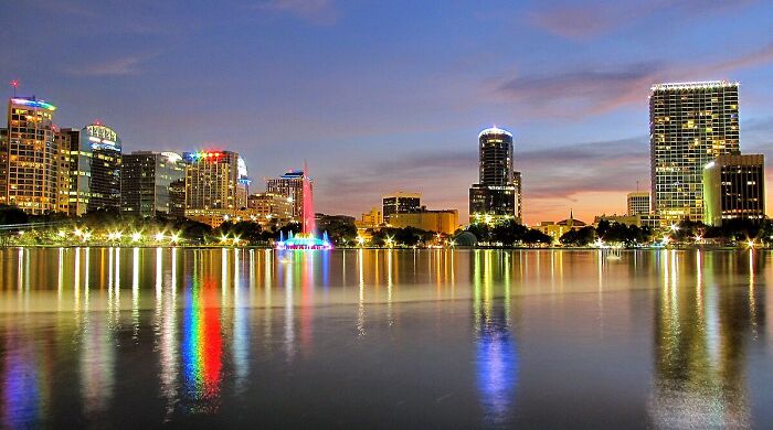 City skyline reflecting on water during sunset, showcasing vibrant night lights.