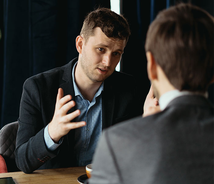 Man in a suit discussing company lunch policy with a colleague in an office setting.