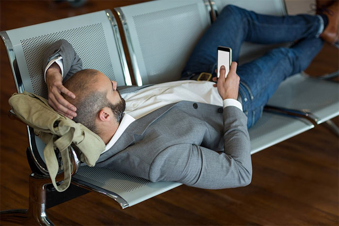 Man in a gray suit relaxing on an office bench, holding a phone, illustrating a potential employee scenario.