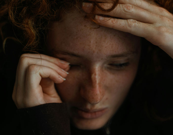 A worried teen with red hair holds their forehead, eyes closed, in an emotional moment related to a mobility cart incident.