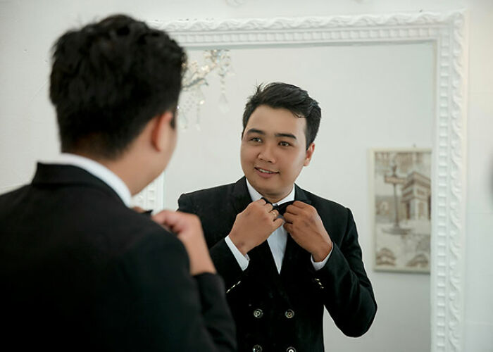 Man adjusting bow tie in front of mirror, demonstrating life hack for perfecting formal attire.