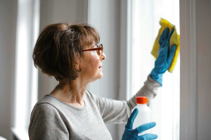 Woman cleaning a window with gloves and a spray bottle, illustrating how buying cleaning tools improved her life.