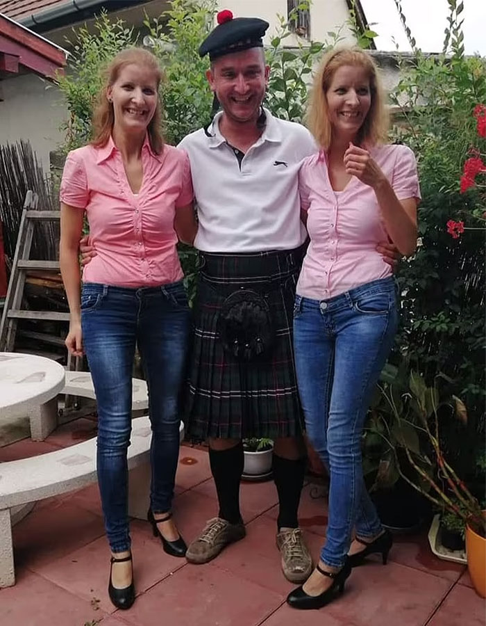 Two women in matching pink shirts and jeans with a man in a kilt, smiling outdoors.