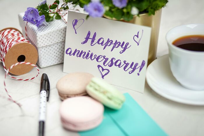 Anniversary card with macarons, signifying a forgiving loving partner, near coffee and gift wrap supplies.