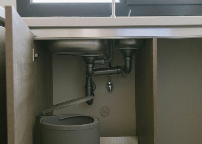 Under-sink storage solution showing organized pipes and a waste bin, illustrating practical life hacks.