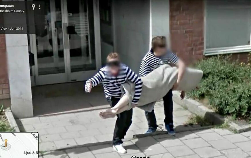 Two people in striped shirts carrying a large carpet on a sidewalk, captured on Google Earth.