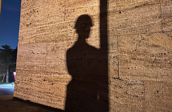 Shadow of a person wearing a helmet cast on a textured wall, symbolizing sacrifice and survival stories shared by people.