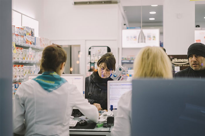People in a pharmacy setting, engaging with staff at the counter.